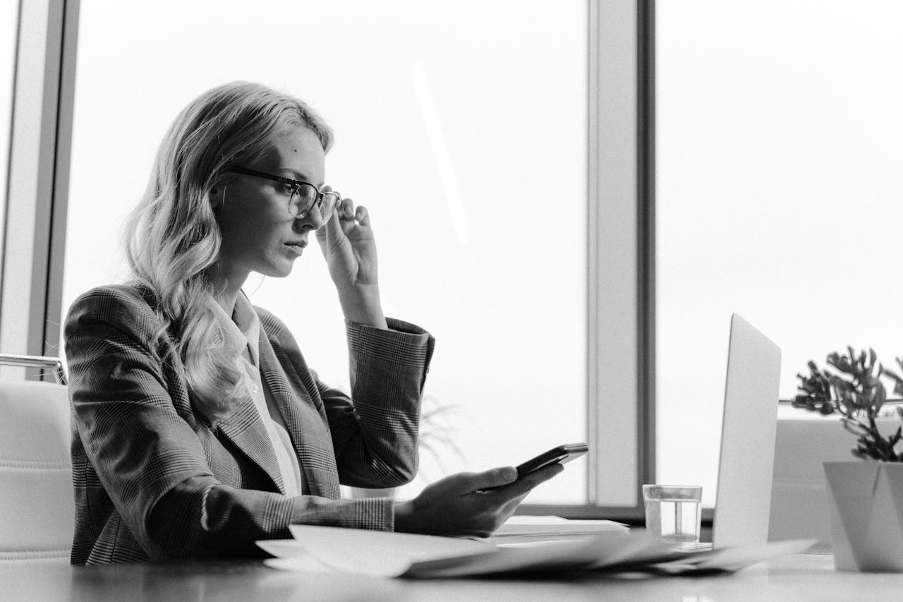 our-services-1 Black and white photo of a businesswoman working with a phone and laptop in a modern office setting.